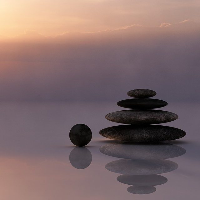 Piedras apiladas y una esfera en un entorno sereno al atardecer.