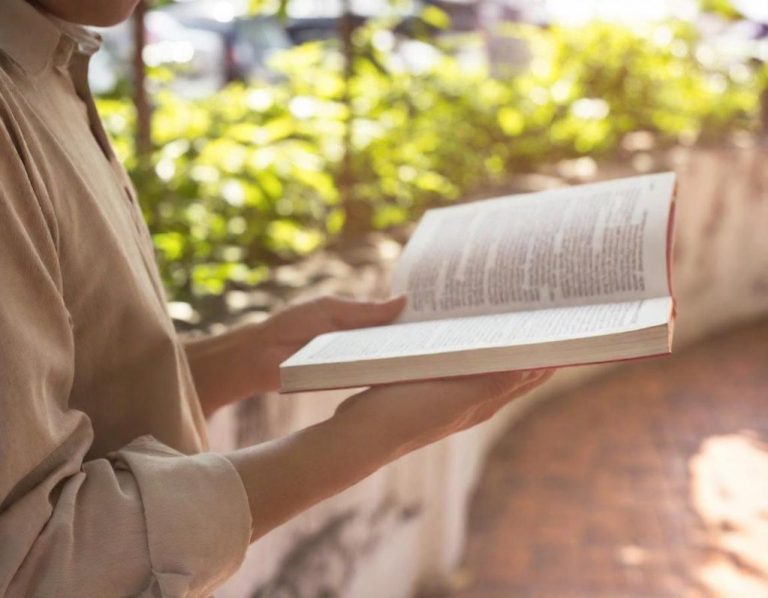 Persona sosteniendo un libro abierto en un entorno exterior con vegetación.